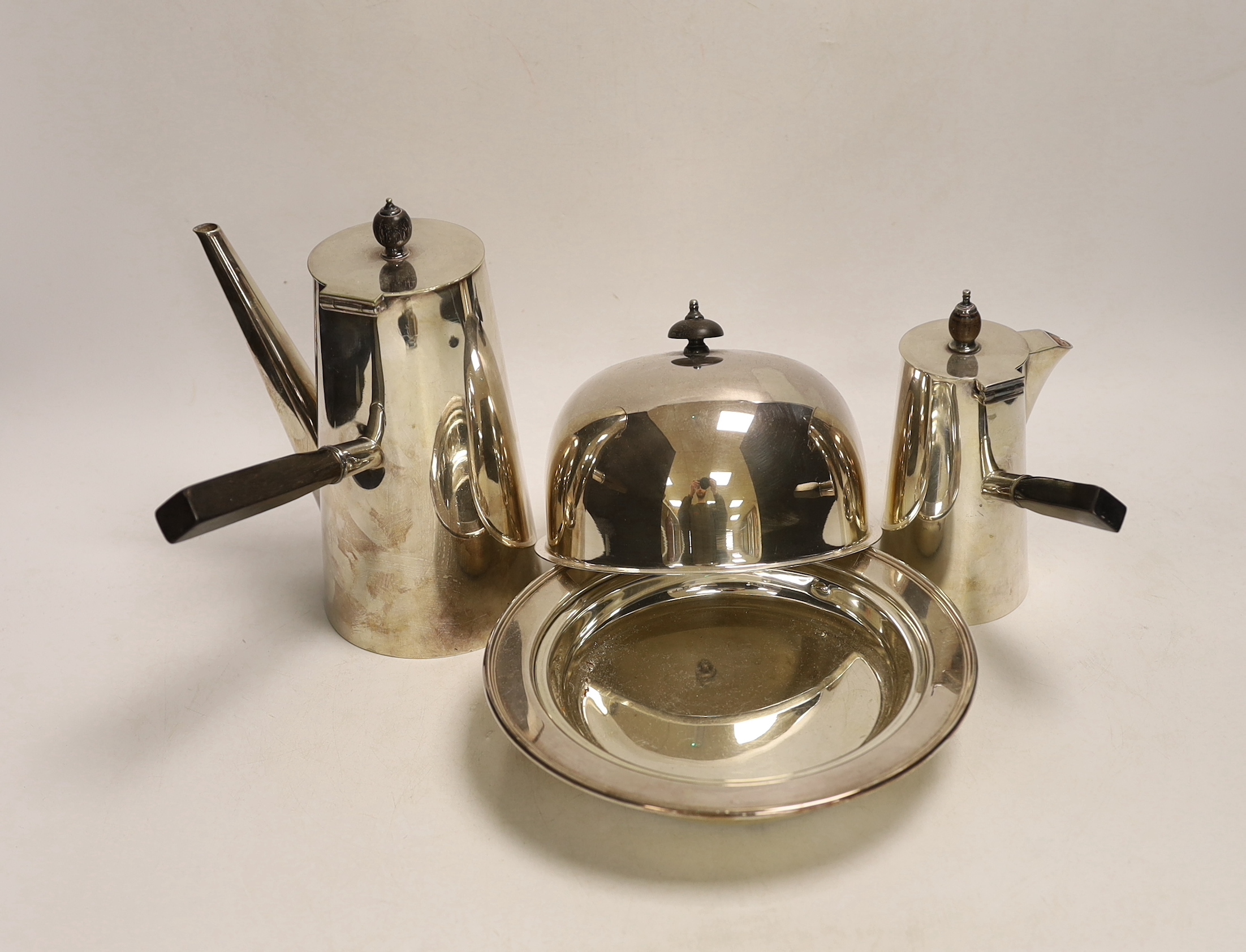 Two silver plated cafe au lait pots, one with double walled interior and a muffin dish, each with ebonised handles, largest 20cm high